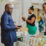 Profissionais conversam em um estande de feira comercial, diante de produtos expostos.