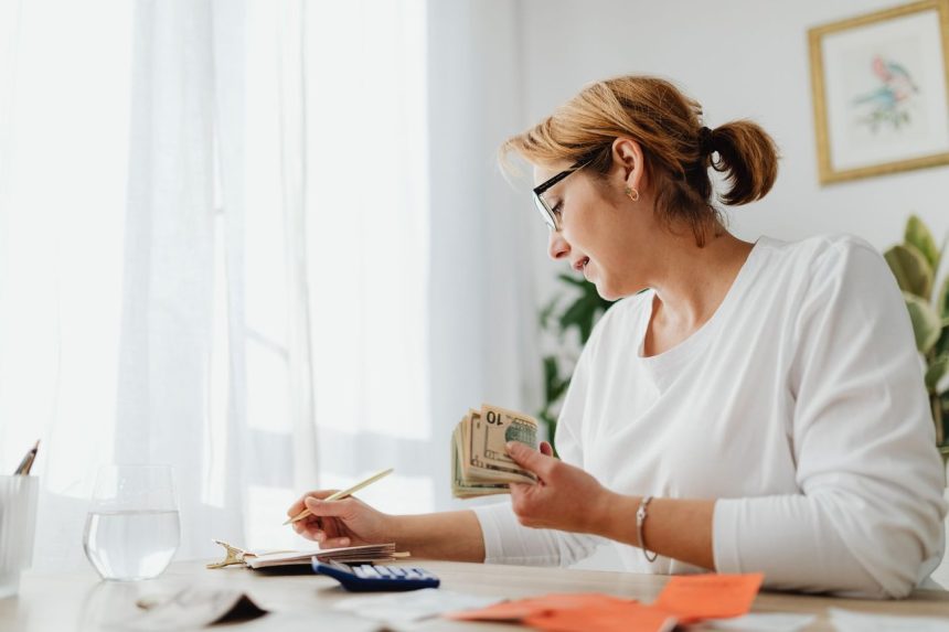 Empreendedora calcula as finanças com dinheiro, calculadora e caderno sobre a mesa.